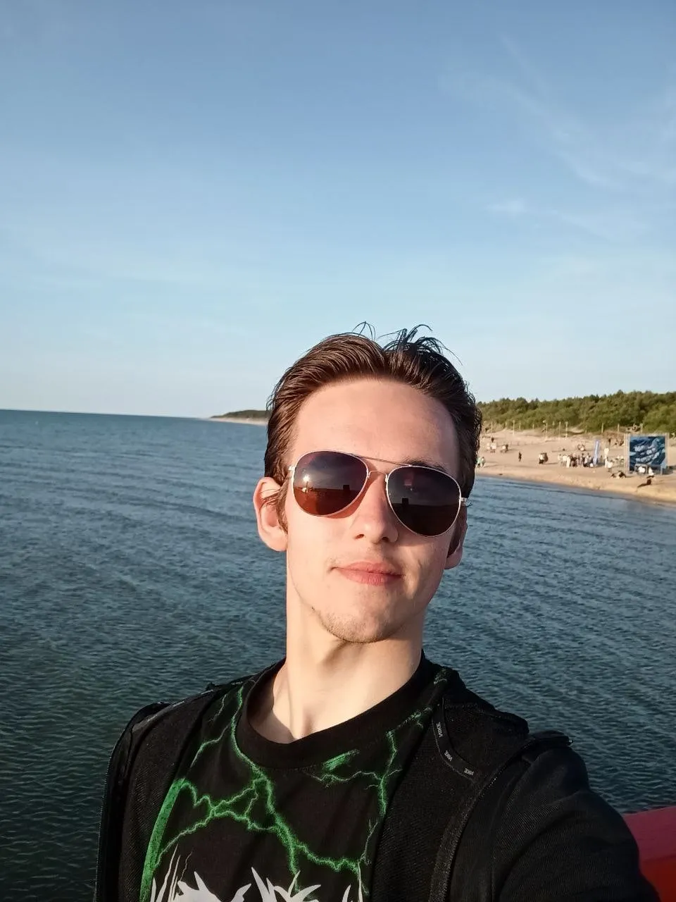 Mateusz Muszarski in sunglasses on a pier, the Baltic Sea and a sandy beach behind him