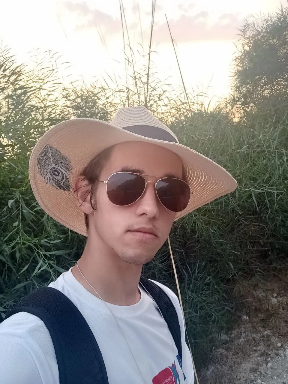 Mateusz Muszarski in a straw hat and sunglasses in front of tall reeds at sunset