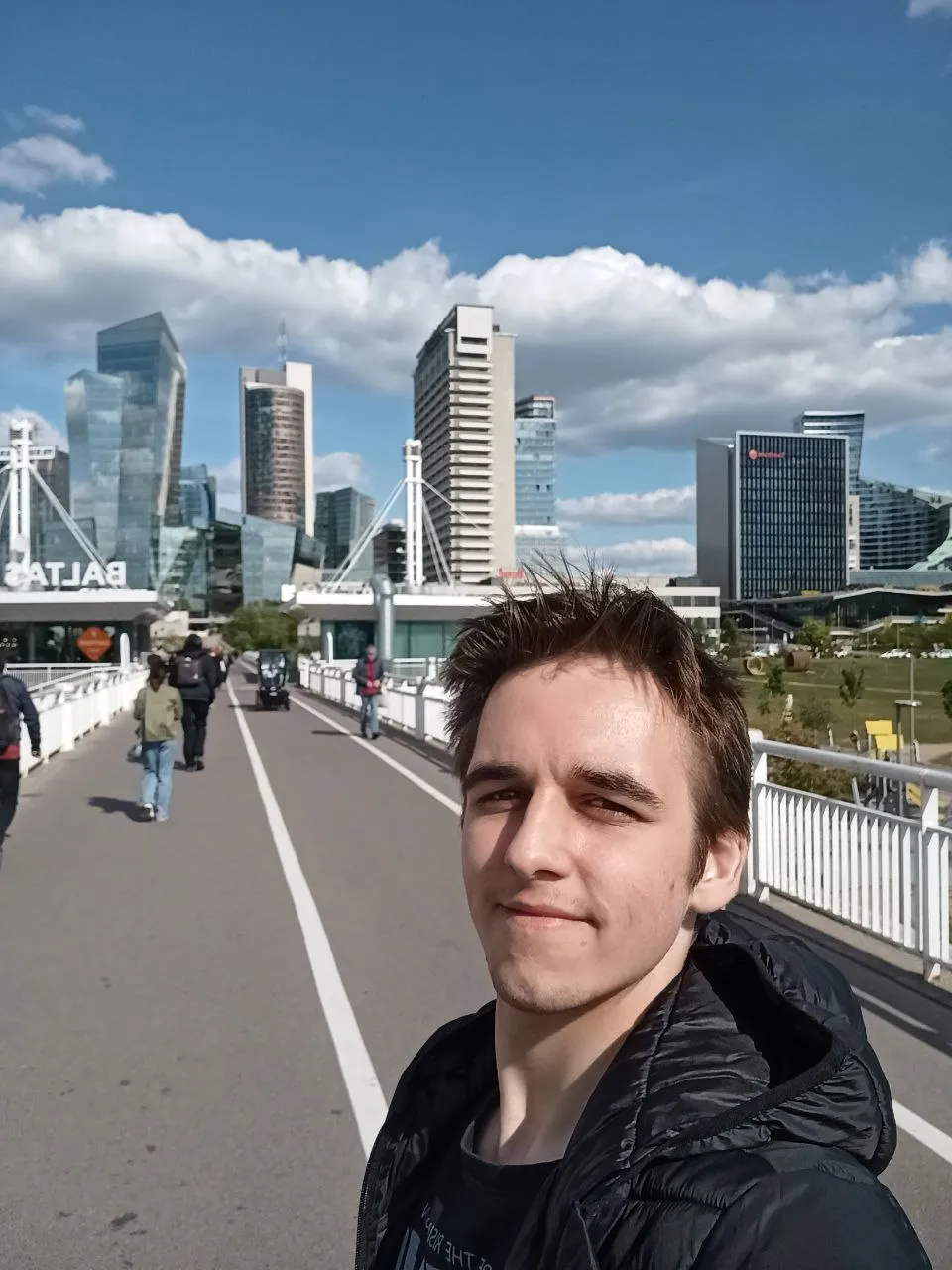 Mateusz Muszarski on a footbridge, glass skyscrapers and a blue sky behind him